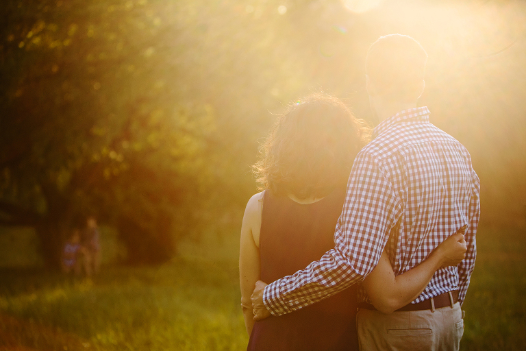 mom and dad watching kids play in field at sunset