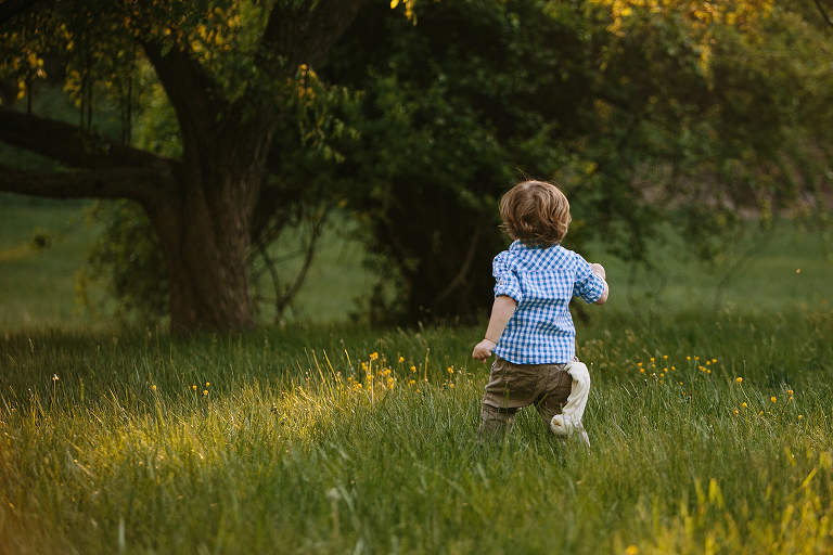 toddler running in field at sunset with stuffed animal in his back pocket