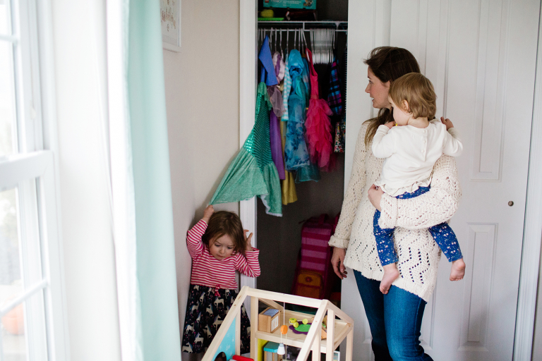 Little girl picking dressup clothes out of her closet with her mom holding her toddler sister