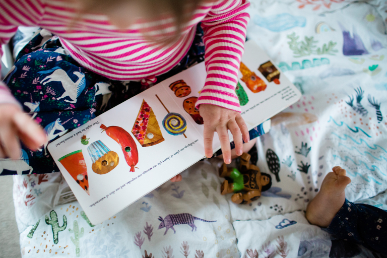 documentary image of preschool age girl pointing to a page in a book she is reading
