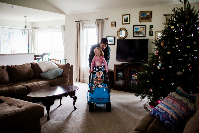 Two sisters being pushed on a toy car in their house by their dad