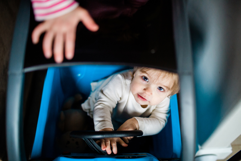 lifestyle image of toddler age girl looking up at camera from inside of a play car