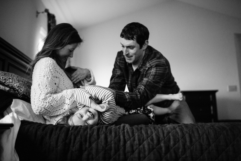 black and white image of mom and dad tickling daughter on bed