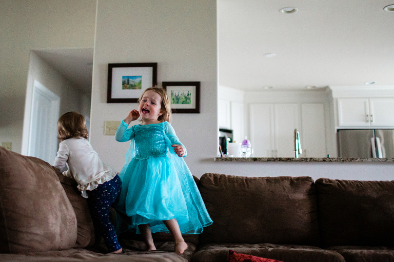 in home family session photo of little girl dressed as elsa singing and dancing on the couch