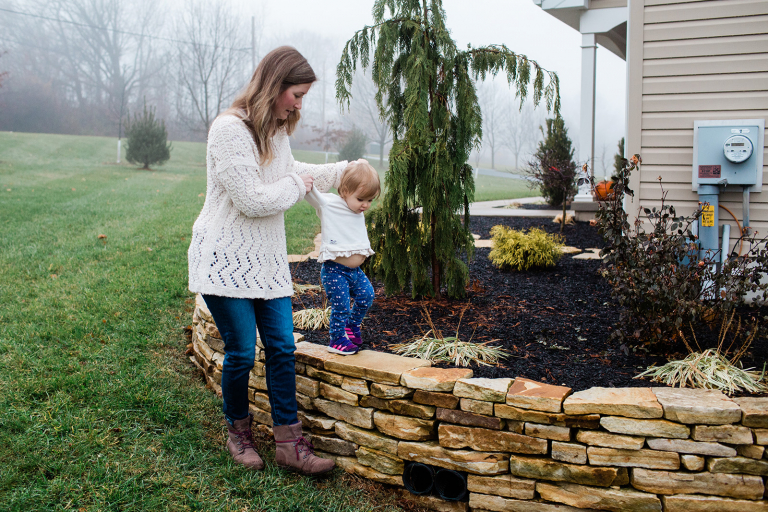 mom helping toddler daughter walk on wall outside