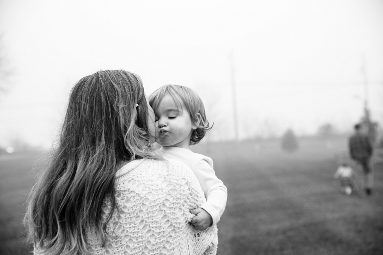 black and white image over mom's shoulder of mom kissing toddler