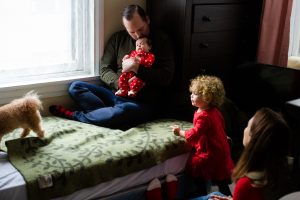 Photograph of family gathered on bed with newborn and toddler girl