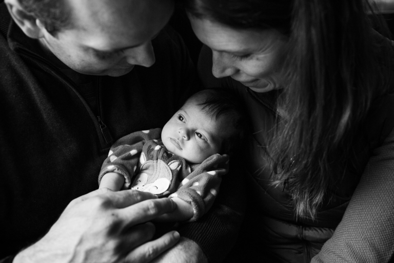 Black and white image of mom and dad gazing down at newborn baby girl