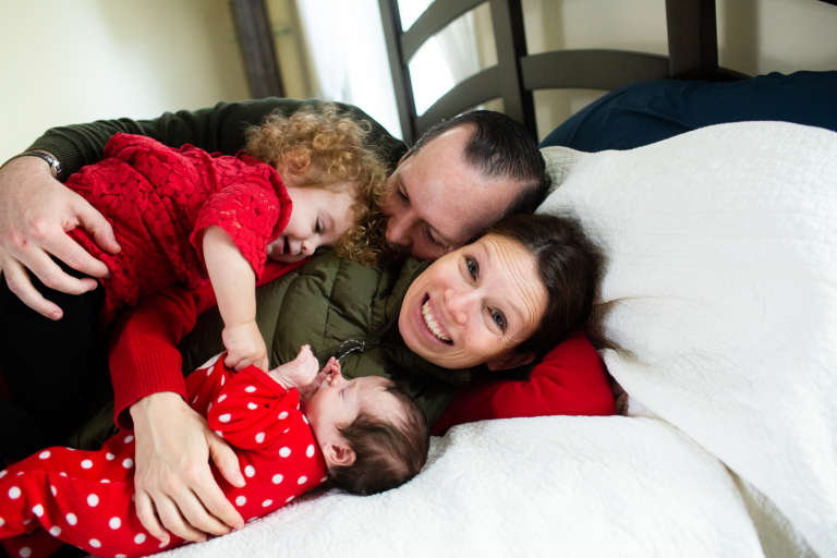 Photograph of family snuggling on the bed with mom looking at the camera