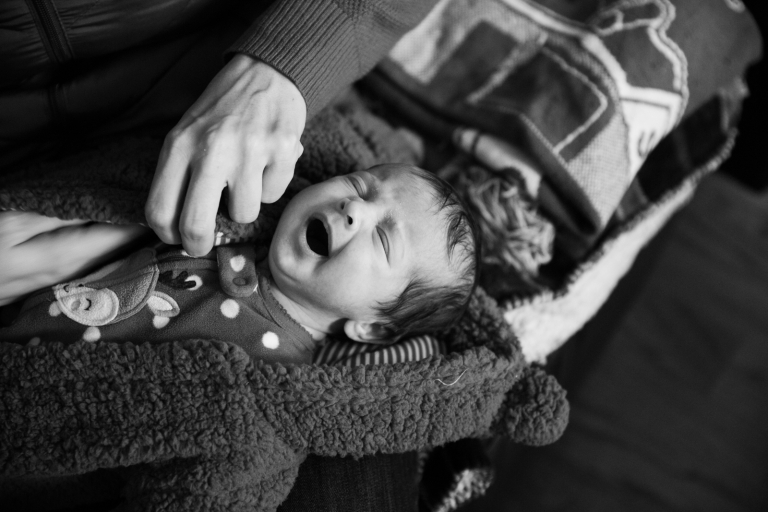 Black and white image of newborn girl yawning while being dressed in winter clothes