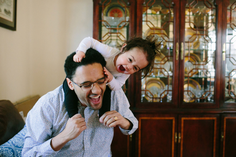 toddler girl sitting on her dad's shoulders and both laughing