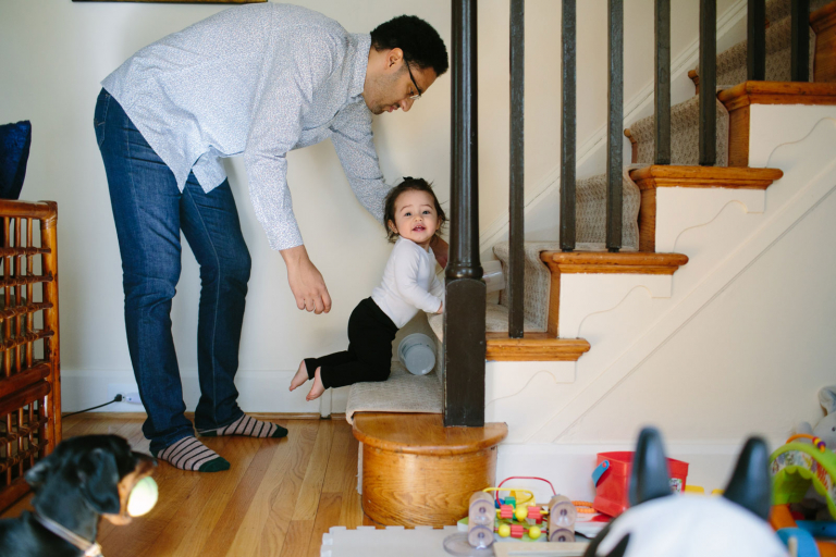 Image of dad helping toddler daughter up the steps as their dog looks on with a tennis ball