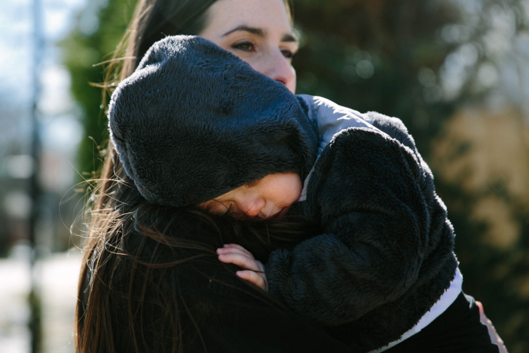 Documentary image of toddler girl snuggling on her mom's shoulder