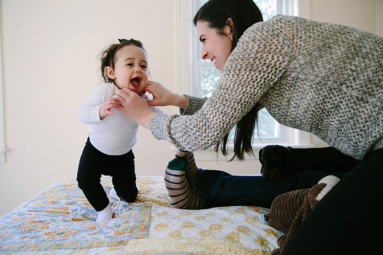 Mom tickling toddler girl on the bed