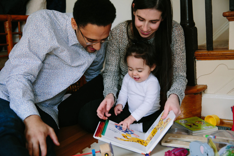 Image of mom and dad reading to their toddler girl