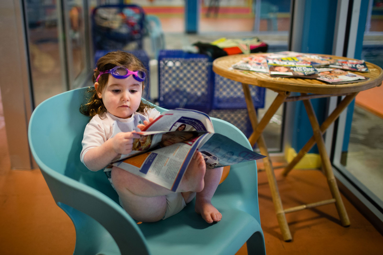 toddler girl reading magazine at Goldfish Swim School in Fort Washington