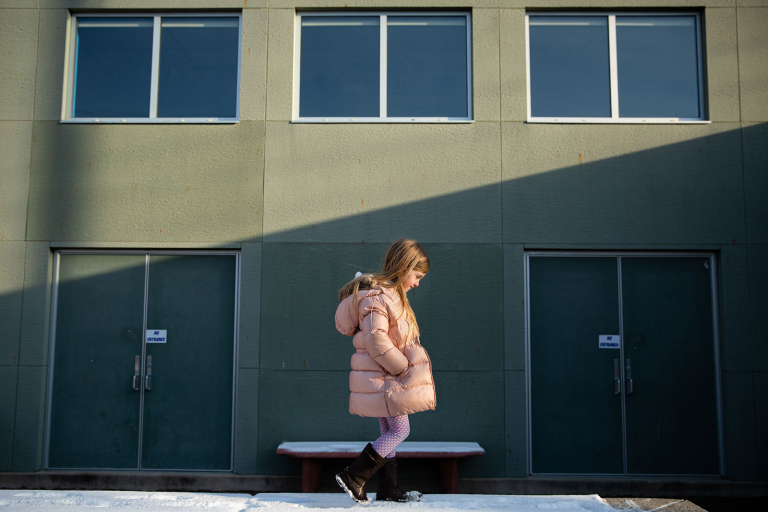 Conshohocken girl walking on wall at elementary school with green wall and windows behind her.