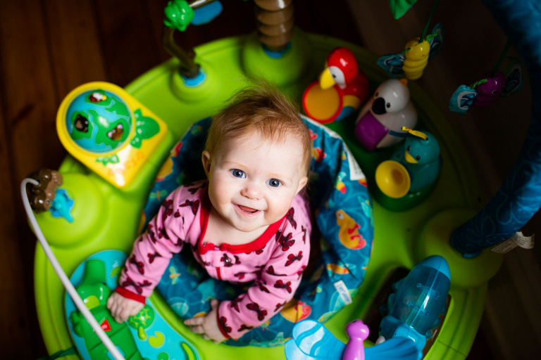 Baby girl in exercauser looking up at the camera.