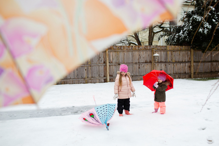 Two girls playing with umbrellas in the snow with umbrella in the foreground.