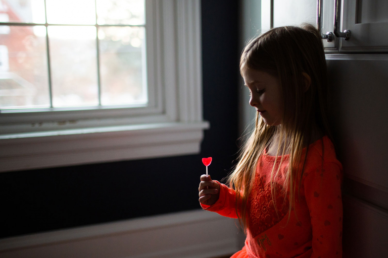 Little girl looking down at heart lollipop with her profile illuminated.