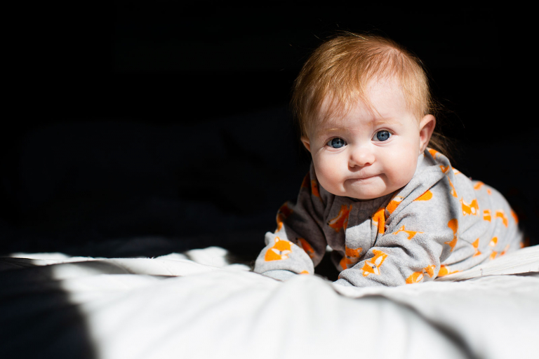 Image of baby girl with red hair and blue eyes in harsh sunlight on bed. 