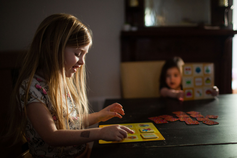 Documentary photograph of two girls sitting at the dining room table playing a game.