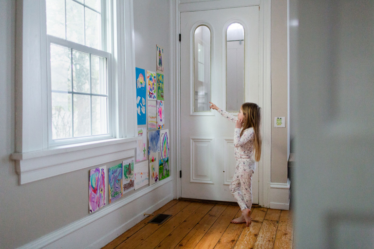 Girl looking at wall of art hanging on the wall in her living room. 