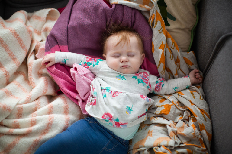 Baby sleeping on a pile of different patterned blankets