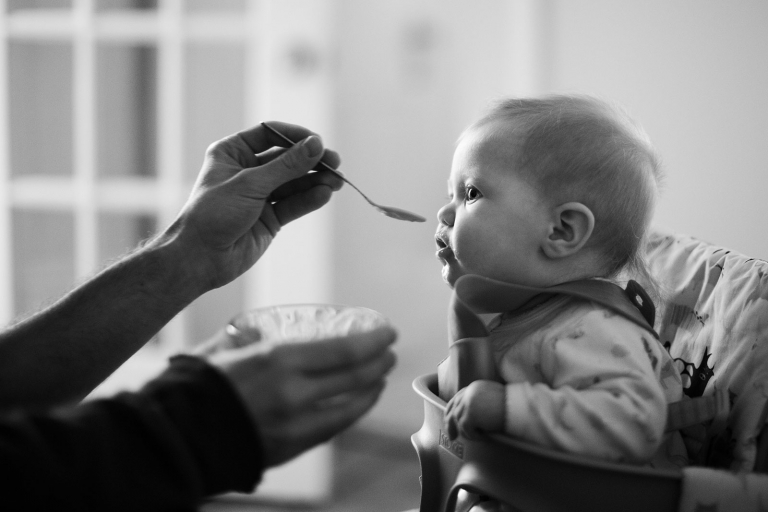Black and white image of baby about to take a bite of a spoonful of food.