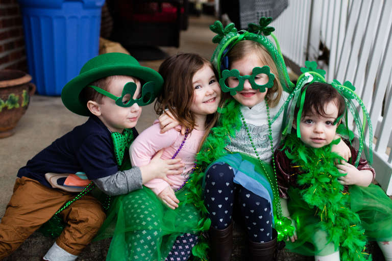 Four kids dressed in saint patrick's day gear sitting on a step and hugging.