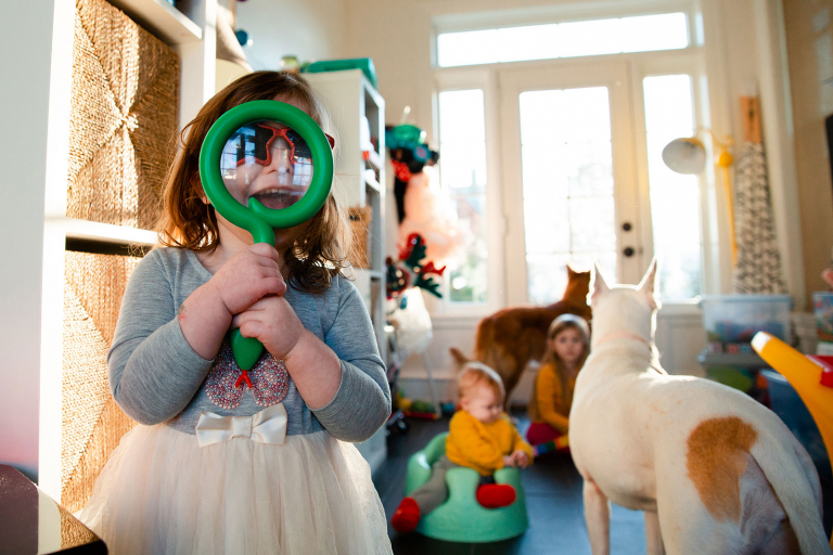Documentary photograph of little girl holding magnifying class with kids and dogs in the background