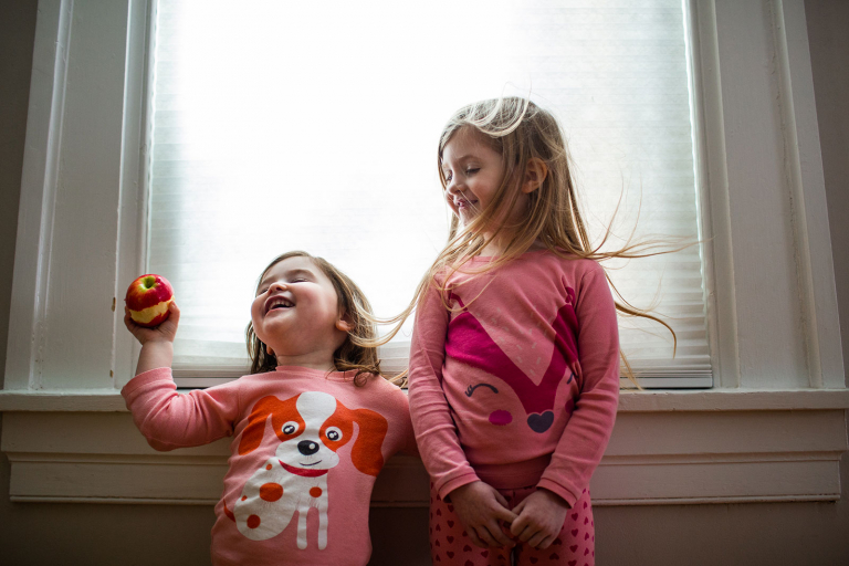 Image of two girls standing in front of a window with their hair blowing