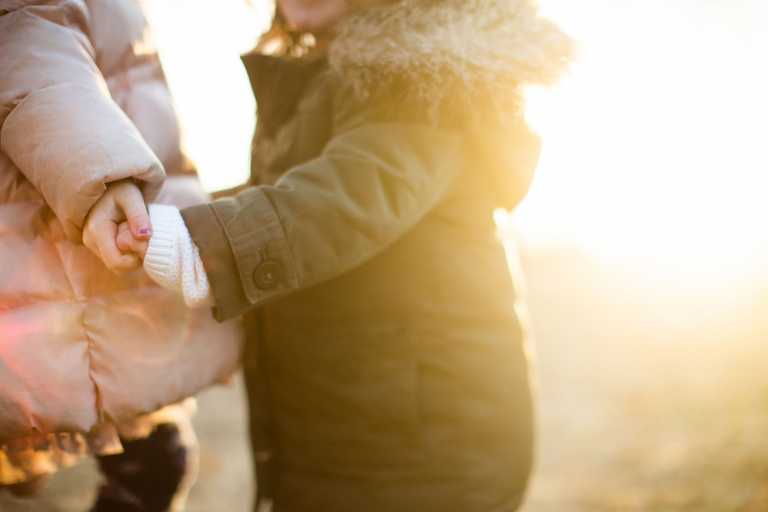 Closeup photograph of two girls holding hands in hazy sunlight