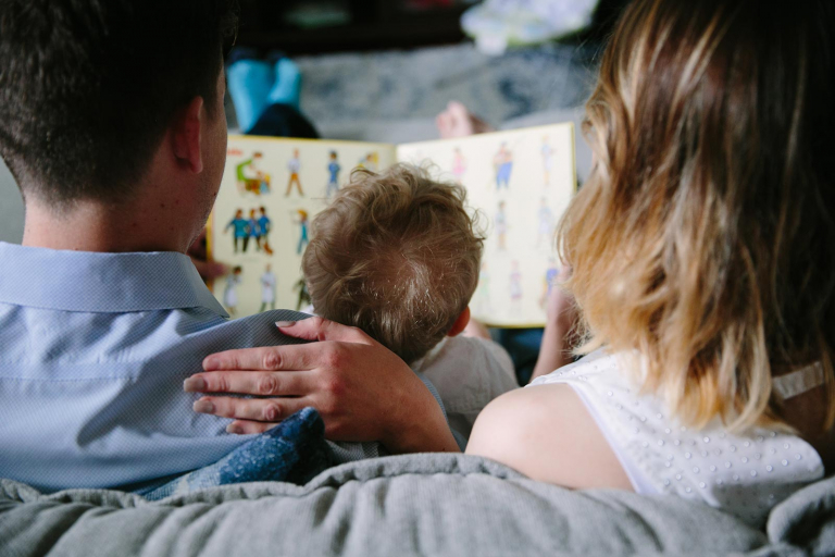 Photograph of the back of little boy and mom and dad as they read a book