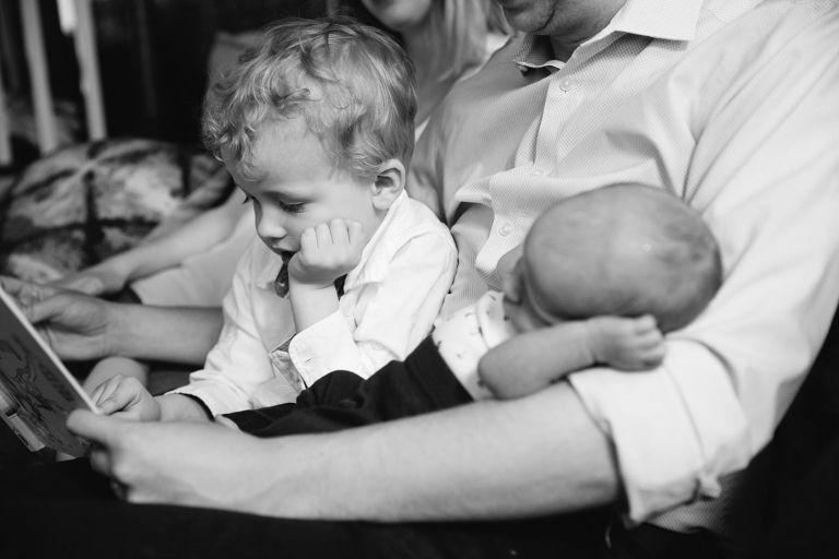 Two boys sitting on dad's lap with hand on cheek the same way