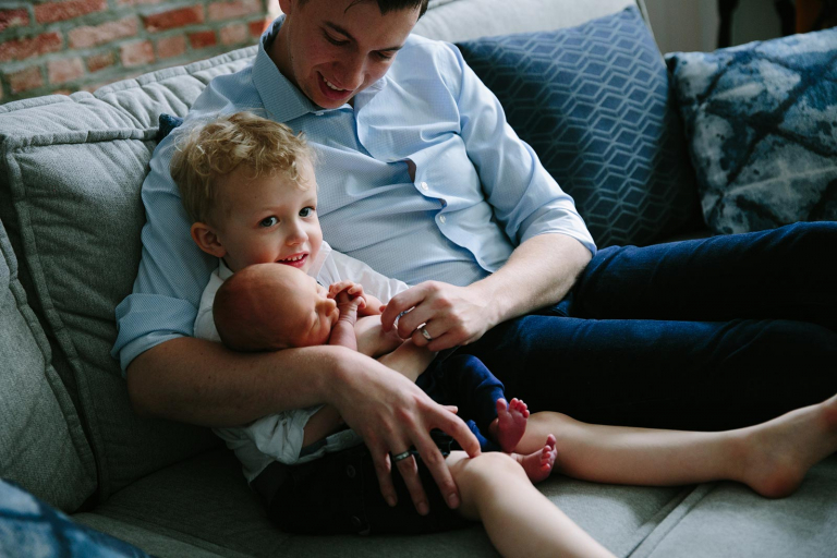 Image of big brother and newborn with dad smiling
