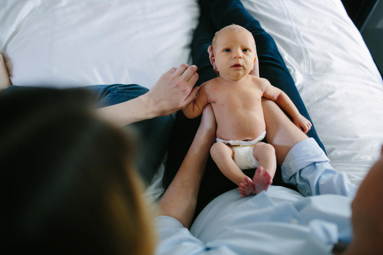 Newborn philadelphia photographer image of baby laying in dad's lap, looking up at the camera
