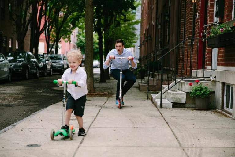 Dad and little boy riding scooters in front of their home