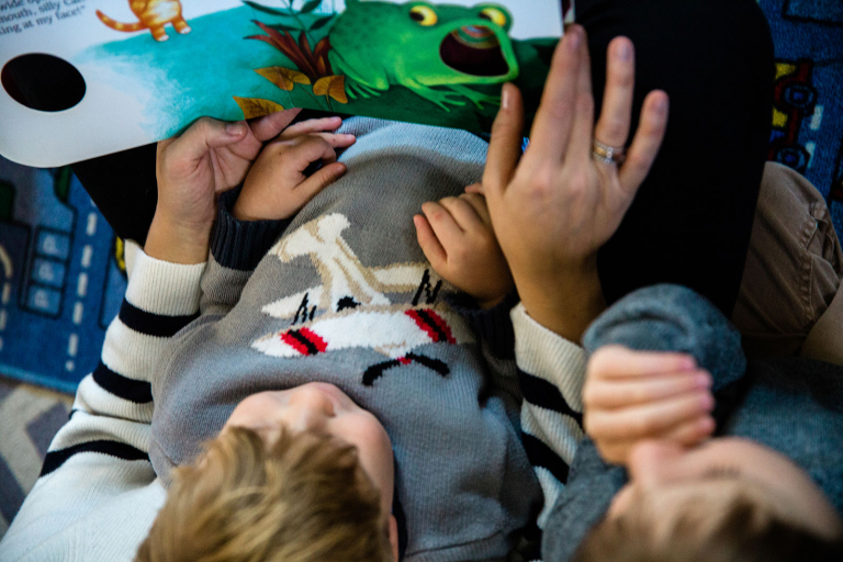 closeup image of hands of mom and two boys reading a book