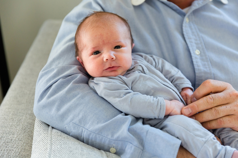 Newborn smiling at camera in dad's arms