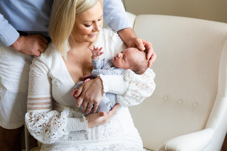 Newborn baby in mom's arms with dad's hand cradling his head.