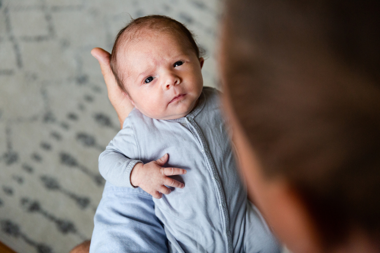 Newborn baby gazing up at camera from dad's hands