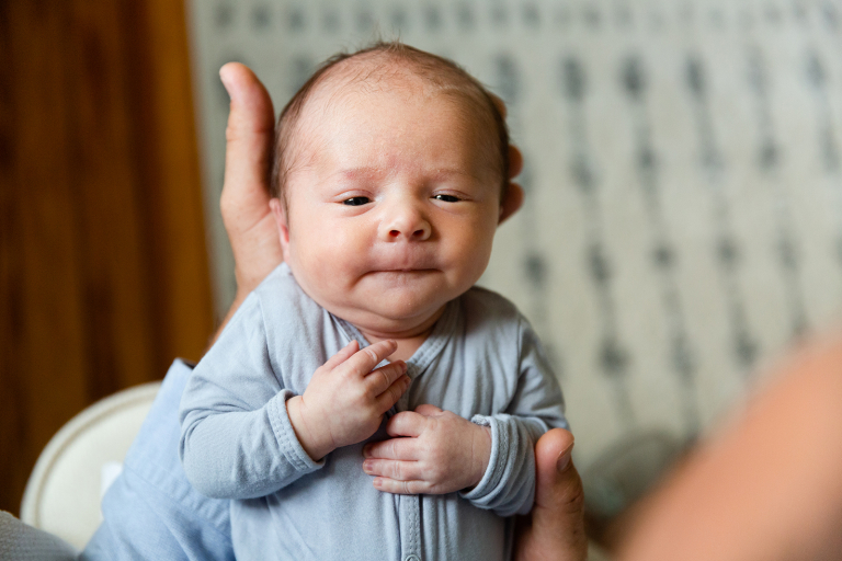 newborn baby smiling up at camera from dad's hands